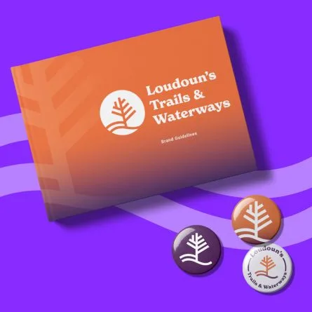 Book titled Loudoun’s Trails & Waterways Brand Guidelines (with an orange cover and orange logo showing a tree outline in orange inside a white circle) with a purple background and three Loudoun’s Trails & Waterways logo buttons (purple, orange, and white).